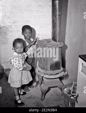 1950S 1960S ZWEI JUNGE AFROAMERIKANISCHE KINDER JUNGE MÄDCHEN SUCHEN BEI DER KAMERA WARM HALTEN DURCH GUSSEISEN HERD SCHLECHTES WOHLERGEHEN GEHÄUSE - N536 HAR001 HARS ALTE MODE SCHWESTER ARMUT 1 JUGENDLICHE KOHLE LEBENSSTIL FRAUEN BRÜDER ARMEN LÄNDLICHEN HEIMAT LEBEN KOPIE RAUM HALBE LÄNGE WOHN MÄNNCHEN KRAFTSTOFF WARME GESCHWISTER SCHWESTERN B&W TRAURIGKEIT BLICKKONTAKT HOCHWINKEL GEFÄHRLICHE WOHLFAHRT AFRO-AMERIKANER AFRO-AMERIKANISCHE SCHWARZE ETHNIE DURCH HÄUSER GESCHWISTER KONZEPTIONELLE WÄRME WOHNSITZ BENACHTEILIGT BABY JUNGE ZUSAMMENARBEIT DESAFFECTED ENTTÄUSCHT ABGEKOPPELT WACHSTUM VERARMTE JUGENDLICHE HALTEN ELENDE NOTWENDIGKEIT ZWEISAMKEIT Stockfoto