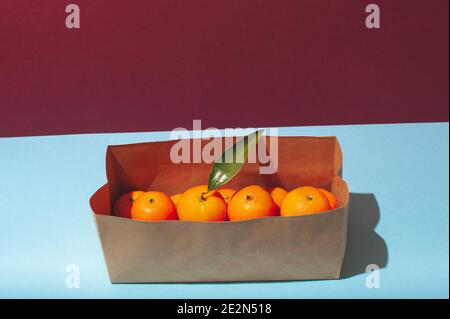 Kreatives Layout mit frischen orangenen Mandarinen im Karton auf dem blauen Pastellhintergrund. Keine Abfallverpackung. Abstraktes Sommer- oder Winterkonzept. Stockfoto