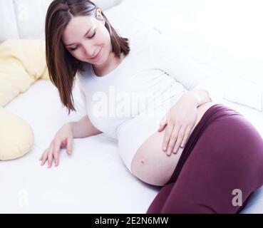 Junge attraktive schwangere Frau im Bett hält ihren Bauch entspannend. Stockfoto