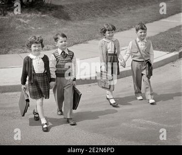 1950ER JAHRE VIER KINDER JUNGEN UND MÄDCHEN ÜBERQUEREN STRASSE AUF IHRE WEG ZUR SCHULE MIT HÄNDEN TRAGEN TASCHE MODISCH GEKLEIDET - S369 HAR001 HARS-STIL TEAMWORK FREUDE LIFESTYLE FRAUEN BRÜDER GESUNDHEIT KOPIEREN RAUM FREUNDSCHAFT VOLLE LÄNGE INSPIRATION MÄNNER WEISE GESCHWISTER SCHWESTERN B&W ZIELE SCHULEN GRAD GLÜCK FRÖHLICH HOHEN WINKEL UND PRIMARY GESCHWISTER LÄCHELT VERBINDUNG KONZEPTIONELL MODISCH FRÖHLICH STILVOLLE ZUSAMMENARBEIT GRAD SCHULWACHSTUM JUGENDLICHE ZWEISAMKEIT SCHWARZ UND WEISS KAUKASISCHEN ETHNIZITÄT HAR001 ALTMODISCH Stockfoto