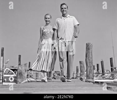 1940ER 1950ER LÄCHELND JUNGE PAAR MANN FRAU IM SOMMER STILVOLL KLEIDUNG, DIE AUF DEM HOLZDOCK AM MOTORBOOT MARINA HÄLT HÄNDE - Y747 HAR001 HARS ALTE ZEIT NOSTALGIE ALTE MODE 1 STIL JUNGE ERWACHSENE TEAMARBEIT URLAUB FREUDE LIFESTYLE ZUFRIEDENHEIT FRAUEN VERHEIRATET EHEGATTEN EHEMÄNNER BOOTE GESUNDHEIT KOPIEREN RAUM FREUNDSCHAFT IN VOLLER LÄNGE PERSONEN DOCK MÄNNCHEN STREIFEN VERTRAUEN TRANSPORT B&W PARTNER BLICKKONTAKT DATING ZEIT WEG GLÜCK FRÖHLICH ABENTEUER FREIZEIT STILE REISE KURZURLAUB LOW ANGLE ERHOLUNG STOLZ HALTEN HÄNDE ATTRAKTION URLAUB LÄCHELT VERBINDUNG BALZ KONZEPTIONELLE BOOTSTOUREN Stockfoto