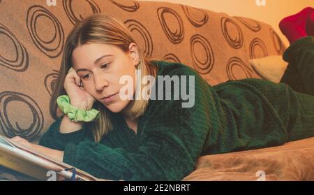 Nahaufnahme eines hübschen Mädchens auf dem Sofa beim Lesen Ein Buch im Schlafanzug mit konzentriertem Gesicht Stockfoto