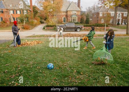 Drei Kinder helfen ihrem Vater, Blätter vom Hof zu säubern Im Herbst Stockfoto