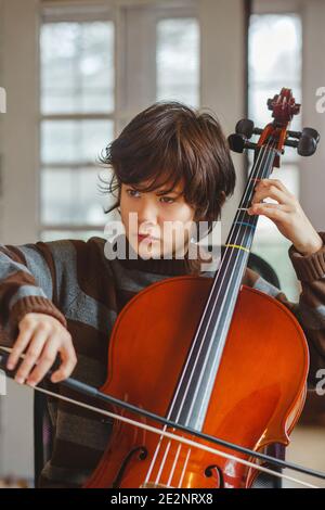 Nahaufnahme des jungen Preteen mit ernsthafteren Gesichtsausdruck, der Cello spielt Zu Hause Stockfoto