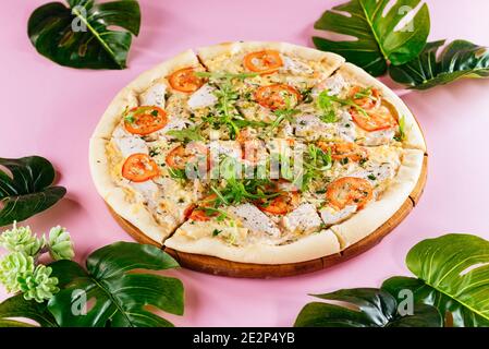 italienische Pizza auf dünnem Teig, rosa Hintergrund mit tropischen Blättern Stockfoto