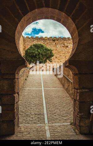 Tor im typisch maurischen Stil mit einer Kopfsteinpflasterrampe, die zu einem Innenhof in der Burg von Trujillo führt. Eine kleine mittelalterliche Stadt in Spanien. Stockfoto