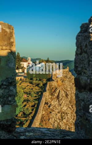 Üppiger Garten und alte Kirche über dem Grat bei Sonnenuntergang, gesehen von Crenel in der Burg von Marvao. Ein erstaunliches mittelalterliches befestigtes Dorf in Portugal. Stockfoto