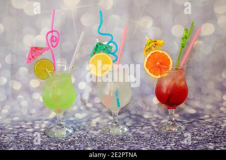 Drei Gläser mit Zitronensaft aus Limette, Grapefruit und lison stehen auf grauem Hintergrund, verziert mit Strohhalmen und Regenschirmen. Nahaufnahme. Stockfoto