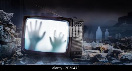 Horror-Foto von einem alten schwarzen gruselig verfolgt tv-Set mit Geisterhand auf dem Bildschirm, auf dunkel neblig ruinierte Stadt mit Geist Figuren Hintergrund stehen. Stockfoto