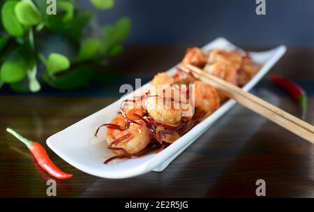 Gegrillte Garnelen mit Zwiebeln und Chili auf einem weißen Teller auf dem Tisch. Für asiatische Gerichte Stockfoto