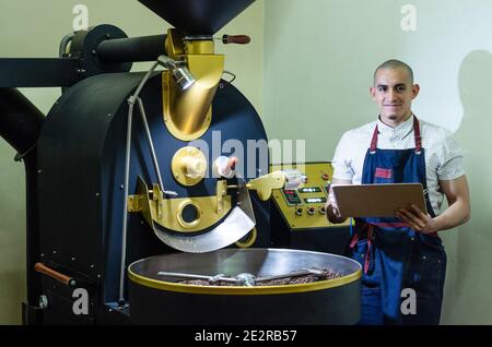 Man's Hands Rösten Kaffee aromatische Kaffeebohnen über eine moderne Maschine zum Braten von Bohnen Stockfoto