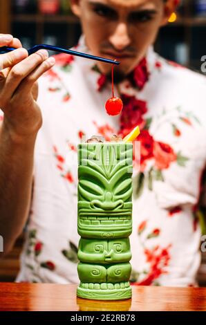 Der Barkeeper bringt eine Kirsche auf einen Tiki-Cocktail Stockfoto