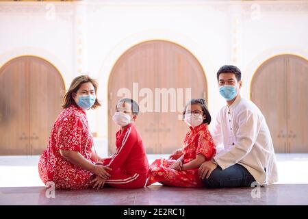 asiatische Familie trägt roten chinesischen Anzug tragen Schutzmaske sitzen Im Freien Stockfoto