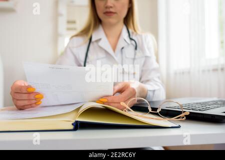 Hält rote Tabletten in der Hand. Arzt im Büro, Online-Beratung. Schreiben auf Notebook. Ein Stapel von Papieren auf dem Tisch. Stockfoto