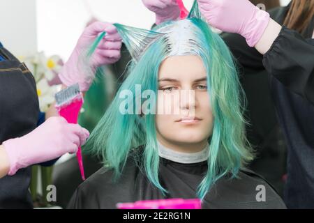 Zwei Friseure verwenden rosa Pinsel beim Auftragen von Farbe auf das Haar während des Prozesses bleichen Haarwurzeln. Nette junge Erwachsene kaukasischen Kunden mit langen Haaren Stockfoto