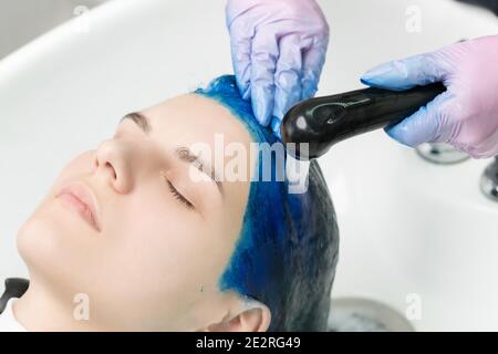 Friseur wäscht den Kopf des Kunden mit Saphir Haarfarbe nach Haarfärbeprozess. Waschen von Haaren mit Shampoo der jungen Frau in Waschbecken Schönheitssalon Stockfoto