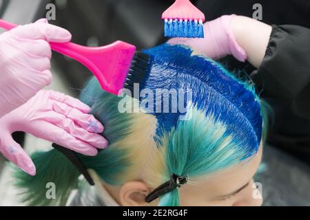 Zwei Friseure mit rosa Pinsel beim Auftragen von blauer Farbe auf weibliche Client mit smaragdgrünen Haarfarbe, während des Prozesses der Färbung Haar im Schönheitssalon Stockfoto