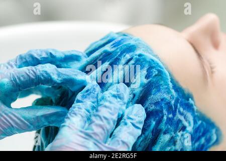 Friseur in Schutzhandschuhen wäscht Kunden blaue Haare mit Shampoo für das Waschen nach dem Prozess der Färbung Haar in schönen Saphir Farbe. Seite V Stockfoto