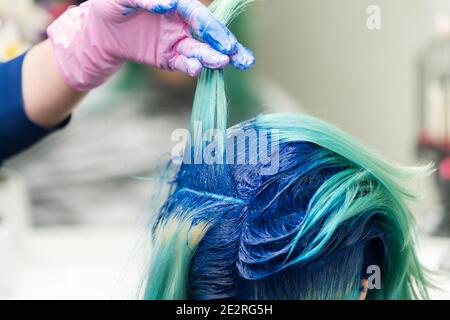 Friseure mit der Hand in schützenden Handschuh heben Schock der blauen Haare des Kunden während des Färbeprozesses im Schönheitssalon. Stockfoto