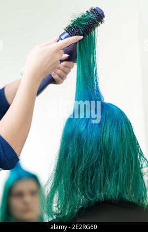 Friseur Kämme und trocknet Haar von smaragdgrünen Farbe mit Haartrockner nach dem Färben Haarwurzeln in Farbe von Lapislazuli. Arbeitet als professioneller Friseur Stockfoto