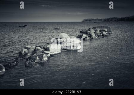 Steine liegen in einer Reihe auf einem Meeresboden in seichtem Wasser, Ostsee Küstenlandschaft, blau getönte monochrome Foto Stockfoto