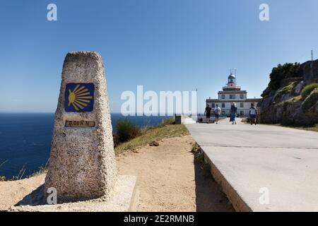 St. James Weg Meilenstein mit gelbem Jakobsschild, Ende der Route, 0.00 km, mit Leuchtturm und Menschen zu Fuß, Kap Finisterre, Galizien, Spanien Stockfoto