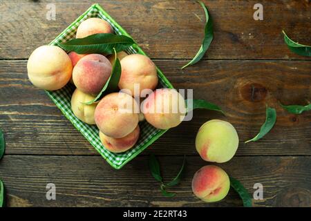 Reife Pfirsiche im Korb auf Holzhintergrund. Hausernte aus dem eigenen Garten. Gesunde Ernährung. Stockfoto