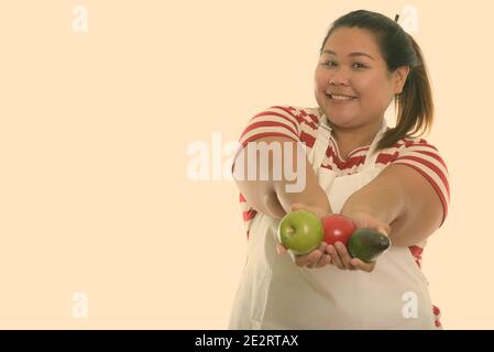Studio shot der Jungen gerne Fett asiatische Frau lächelnd, während Sie eine frische Früchte und Tragen einer Schürze Stockfoto