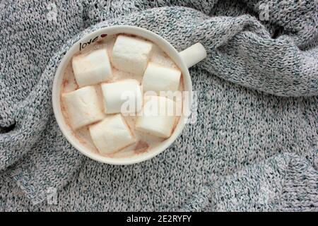 Ansicht von oben auf einer großen Tasse heißen Kakaos mit Salmler auf einem grauen Strickpullover-Hintergrund. Gemütliches Winterkonzept. Draufsicht Stockfoto
