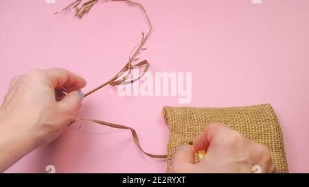 Floristen Hände bereiten trockenes Gras und Segeltuch Tasche für die Komposition, auf rosa Hintergrund, DIY-Konzept. Stockfoto