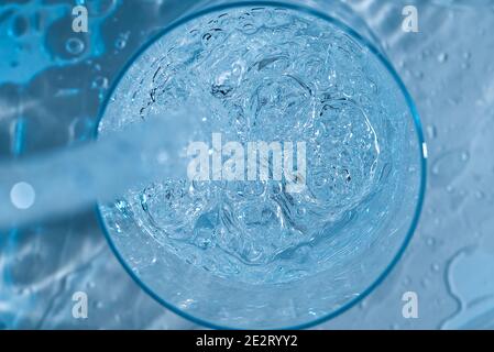 Sauberes Trinkwasser aus blauer Plastikflasche in Glas gießen Auf blauem Hintergrund Stockfoto