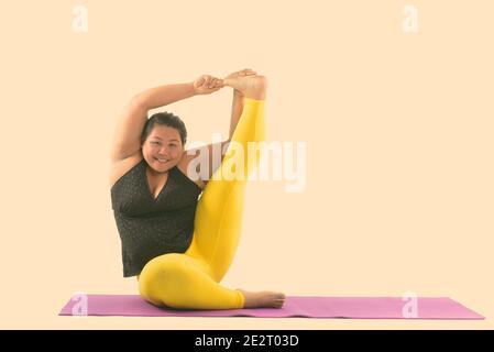 Studio shot der Jungen gerne Fett asiatische Frau lächelnd und Ihr linkes Bein während Yoga Posen Stockfoto