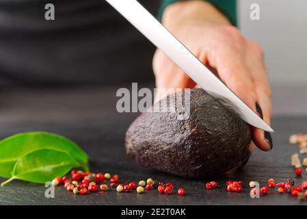 Der Koch zerschneiden die Avocado-Nahaufnahme auf einem schwarzen Brett Stockfoto