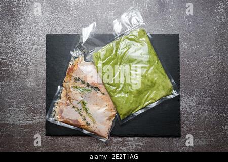 Produkte in Vakuumverpackung auf schwarzem Schiefertafel. Hühnerfleisch mit Kräutern und grünen Bohnen pürieren, vakuumversiegelte Lebensmittel bereit für Sous Vide Kochen. Sous Stockfoto