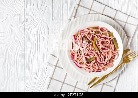 Deutscher Wurstsalat Wurstsalat aus geschnittener lyoner-Wurst mit Gurken Und rote Zwiebel serviert auf einem weißen Teller mit goldenen Besteck und Serviette auf einem weißen Stockfoto