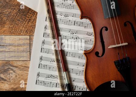 Geige, Noten und Bogen lagen auf einem hölzernen Hintergrund. Weiche Schatten. Stockfoto