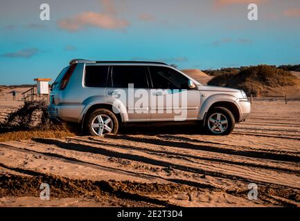 SUV auf dem Sand in der Nähe eines Ufers unter einem geparkt Sonnenuntergang Himmel Hintergrund Stockfoto