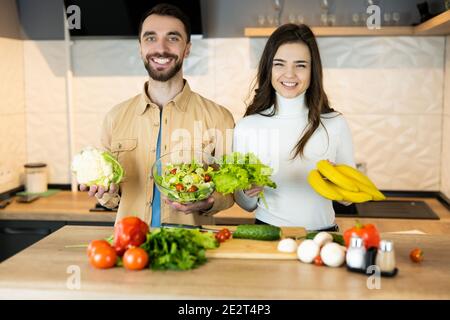 Junge und schöne vegetarische Paare lächeln in der Küche während des Kochens. Auch sie sehen glücklich und gesund aus, weil sie nur Ernährung und f verwenden Stockfoto
