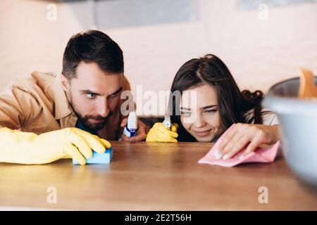 Glückliches Paar macht Hausreinigung in der modernen Küche zu Hause. Nahaufnahme von jungen Mann und Frau Waschtischplatte mit Waschmittel und Tuch mit Frau waschen Stockfoto