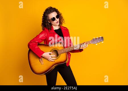 Portrait von attraktiven talentierten beliebten wellig-haarigen Mädchen spielen Bass-Gitarre Isolierter hellgelber Hintergrund Stockfoto