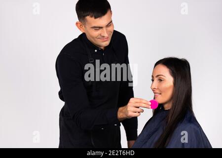 Geschlechterstereotypen. Männlich Make-up Künstler wischt Gesicht mit Make-up Schwamm. Weißer Hintergrund. Stockfoto