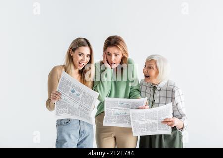 Drei Generationen staunende Frauen, die auf Weiß isolierte Zeitungen lesen Stockfoto