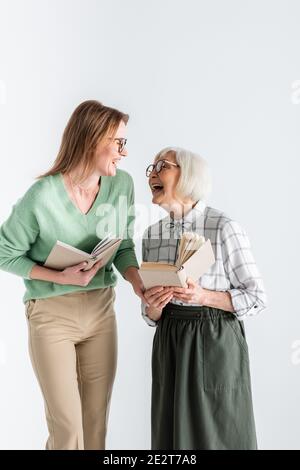 Ältere Mutter lacht mit Tochter in Brille, während sie Bücher hält Isoliert auf Weiß Stockfoto