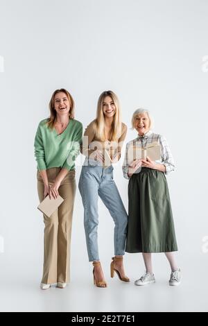 Volle Länge von drei Generationen von glücklichen Frauen mit Büchern Auf Weiß Stockfoto