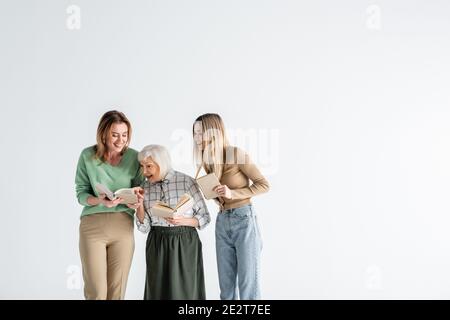 Drei Generationen glücklicher Frauen, die Bücher halten und isoliert lächeln Auf Weiß Stockfoto