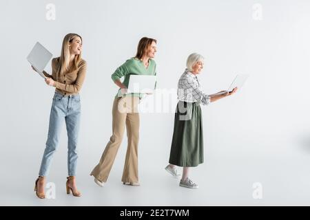 In voller Länge von drei Generationen von fröhlichen Frauen mit Laptops Auf Weiß Stockfoto