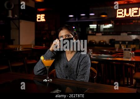 Porträt einer Frau, die Gesichtsschutz Maske trägt, während sie in einem Restaurant sitzt. Stockfoto