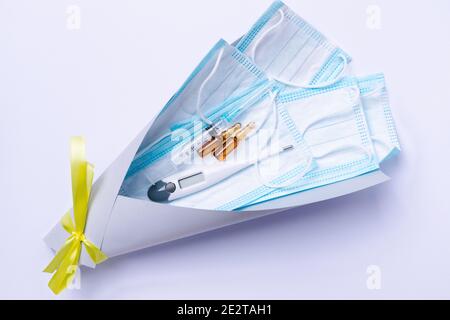 Das aktuellste Kit während einer Pandemie. Medizinische Schutzmasken, Thermometer, Spritze und Ampullen in einem Bouquet auf weißem Hintergrund. Stockfoto