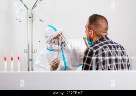 Medizinisches Personal, das COVID-19 Test durchführt, nasale Abstrichprobe vom männlichen Patienten im Krankenhauslabor nimmt, PCR-Diagnostik für Coronavirus, Doktor in PPE usi Stockfoto