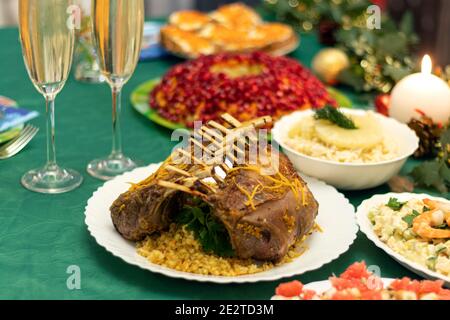 Ein festlicher Tisch mit vielen leckeren Gerichten. Lammkarree, zwei Gläser Champagner, Salate und Snacks auf dem festlichen Tisch. Feiern zu Hause. Weiche Fo Stockfoto
